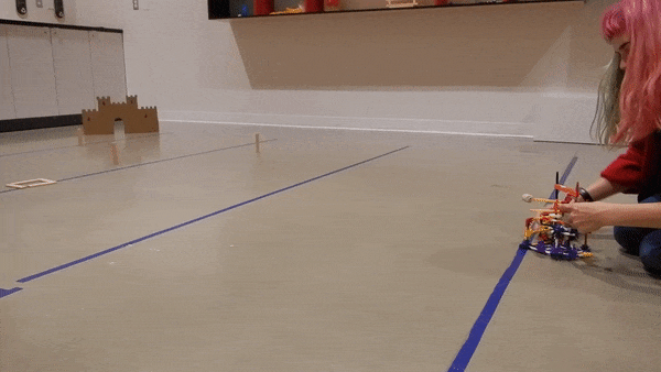 A cork is fired from a sideways K’NEX catapult towards a cardboard target. The cork flies only a couple of centimetres.  