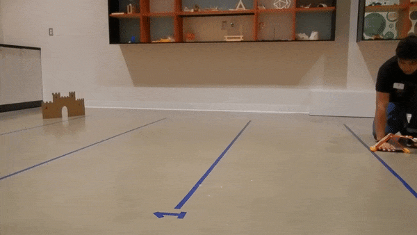 A cork is fired from a K’NEX catapult towards a cardboard target. The cork flies high above the target, missing completely.  