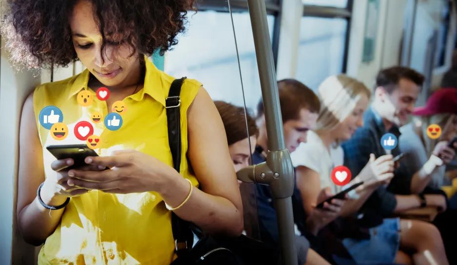 Woman in a yellow shirt looks at her smartphone, while standing on a subway 