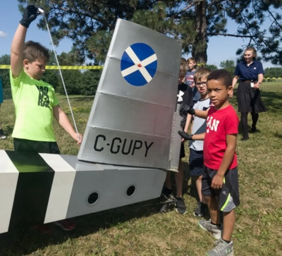 A group of children inspect and measure the tail of the plane.