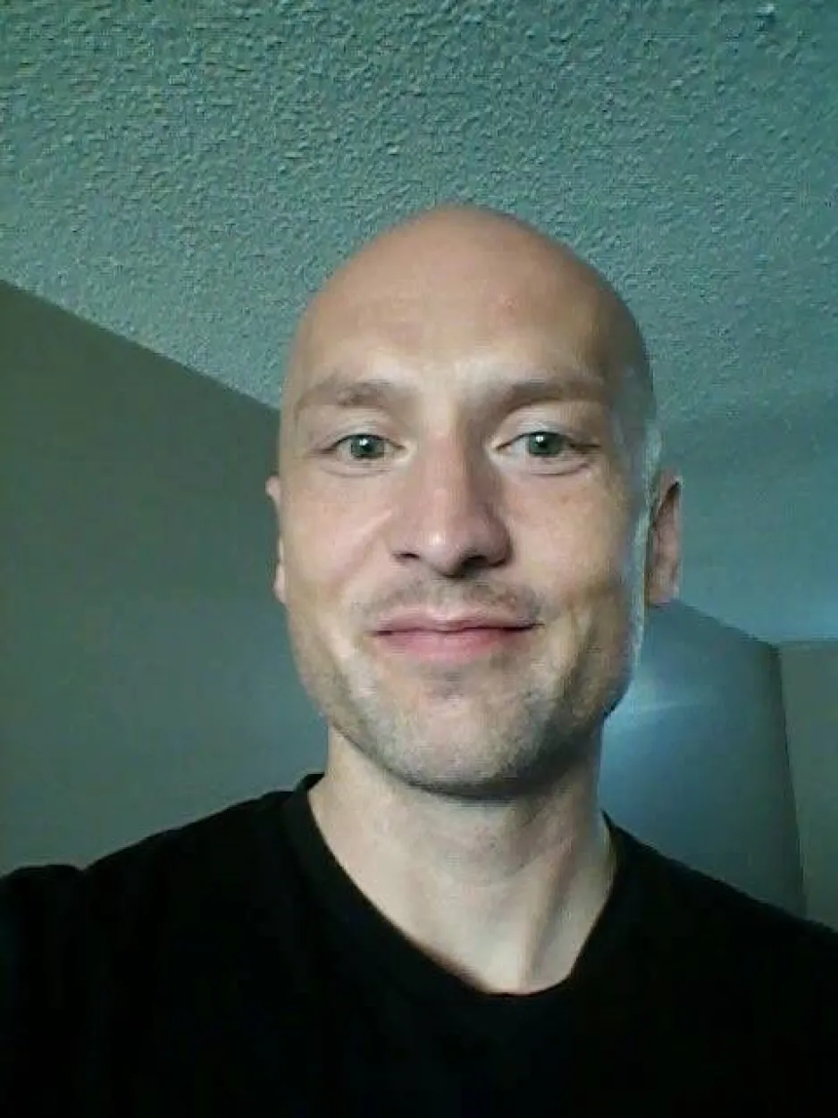 A man in a black t-shirt smiles at the camera.