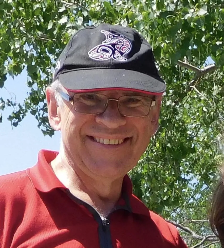 Un homme portant un chandail rouge et une casquette sourit chaleureusement à la caméra.