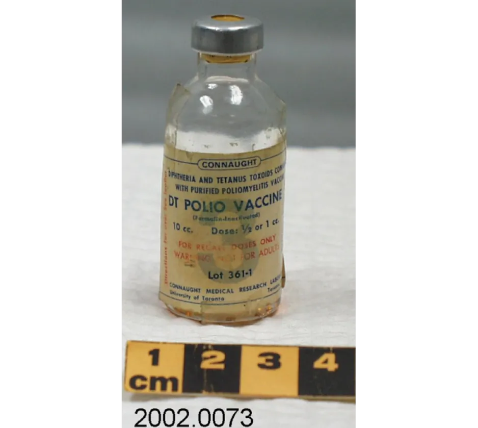 A tiny, clear glass vial of polio vaccine sits on a white piece of fabric. The blue and red writing is faded; in blue writing, the largest text reads: “DT POLIO VACCINE.”