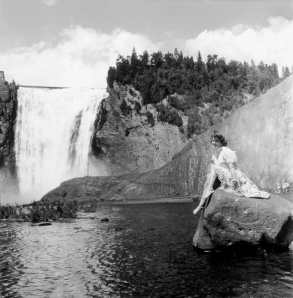 Photographie en noir et blanc d’une vue panoramique des chutes de Montmorency à Québec.  Les chutes sont visibles du côté gauche de la photographie et une femme est assise sur un rocher du côté droit.