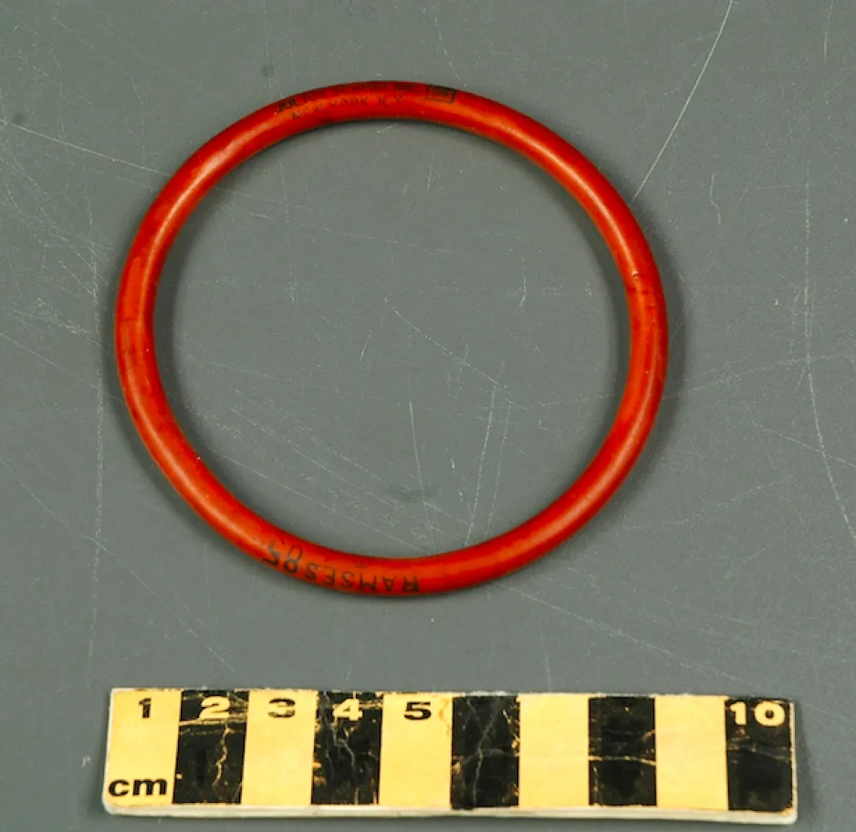 Élastique circulaire de couleur orange brûlé, de moins de 1 cm d’épaisseur et d’environ 8 cm de diamètre.