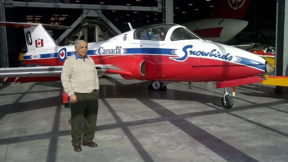 A colour image depicts a Black man standing in from of a single engine jet aircraft.  The aircraft has the Canada wordmark as well as ‘Snowbirds’ written on it.