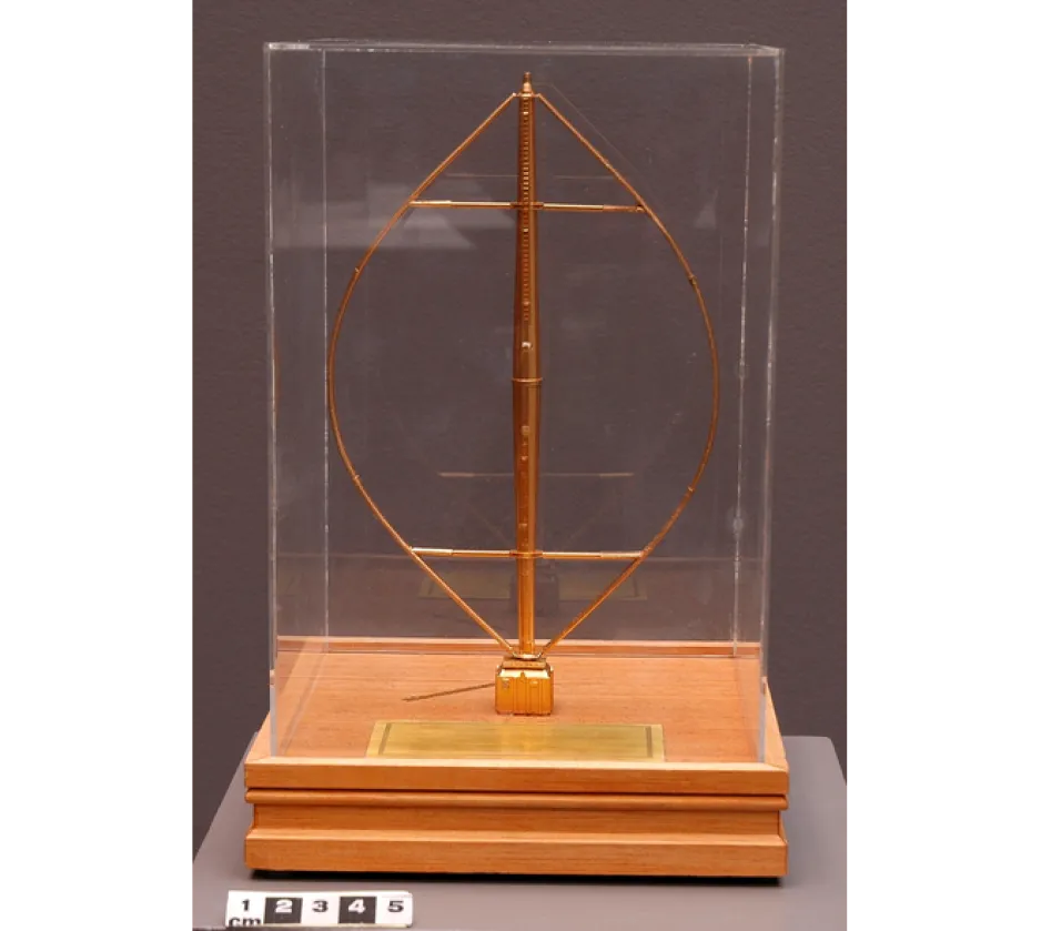 Gold tone synthetic model of a vertical axis wind turbine mounted on square wooden base.