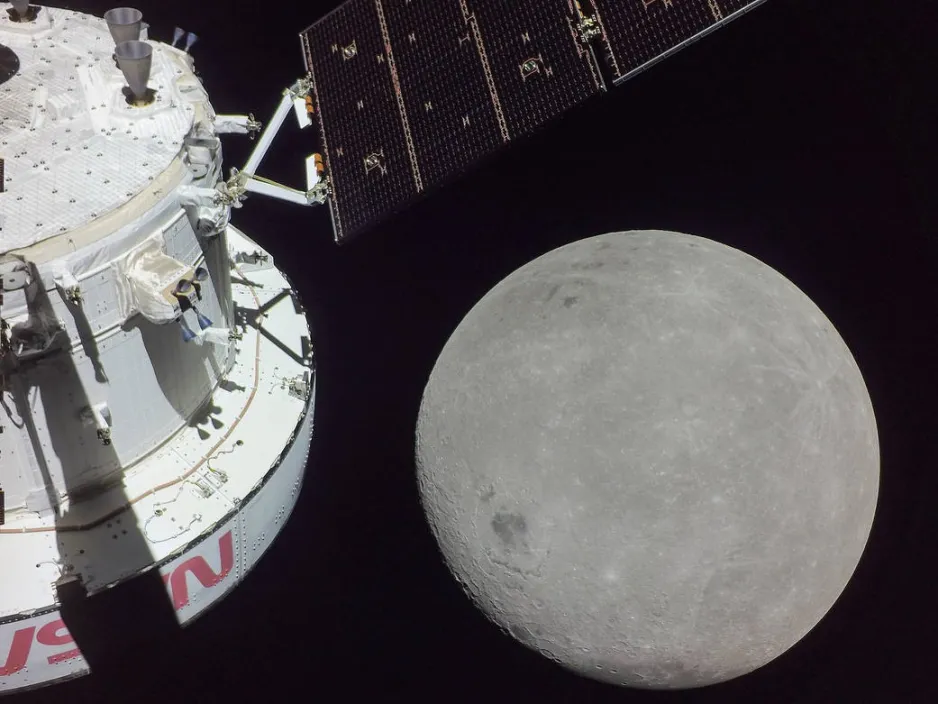 On voit l’astronef Orion à gauche avec une vue de la face cachée de la Lune à droite, le tout contre un arrière-plan noir.