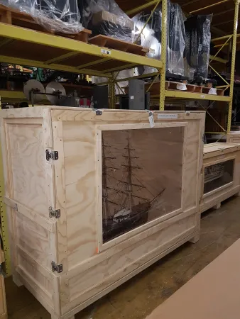 A large wooden crate displays a ship model through a clear panel.