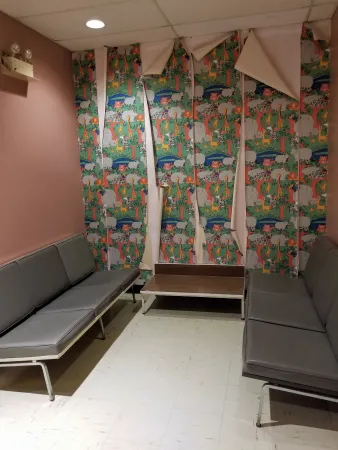 A small room with two benches on opposite walls. The back wall has 6 panels of children's wallpaper that is peeling off.