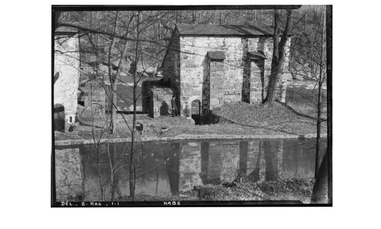 A black-and-white photograph shows stone brick buildings on a riverbank.