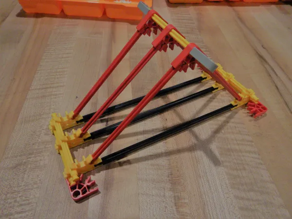 A completed catapult base made out of K’NEX. A square base with a pyramid built above it. 