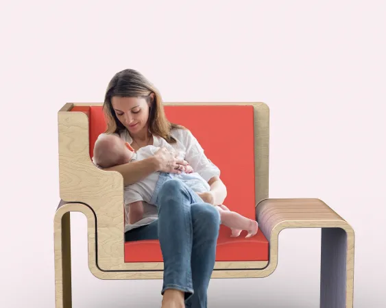 Une jeune femme allaite un bébé, assise dans un fauteuil d’aspect moderne avec un siège orange.