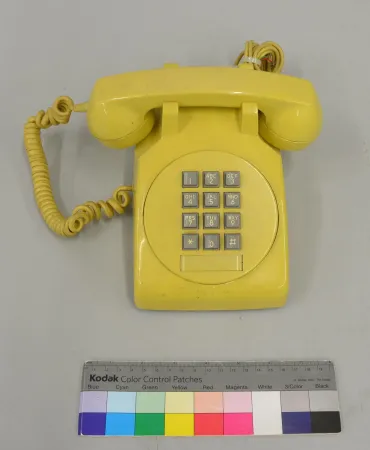 A lustrous, bright yellow desk phone with grey keys sits on a grey background. 