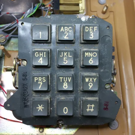 The exposed dark grey plastic keypad of the brown desk phone, with white lettering, soiled. 