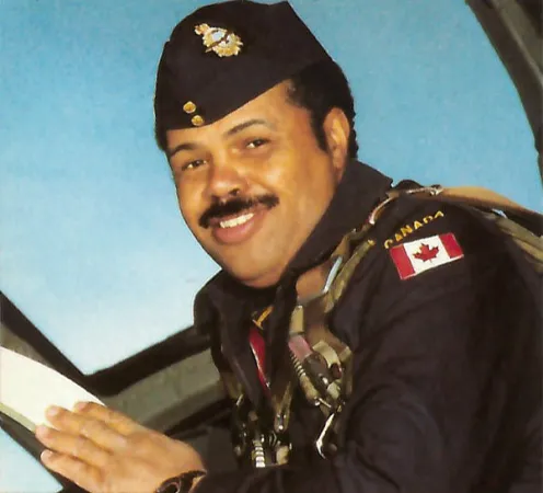 A colour image depicts a Black man in an aviator uniform posing inside the cockpit of an aircraft.