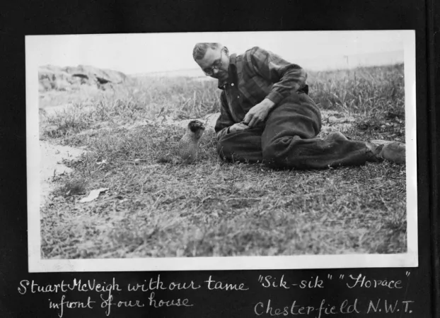 Photographie horizontale en noir et blanc d'un homme portant des lunettes allongé sur le sol qui nourrisse à la main un petit écureuil.