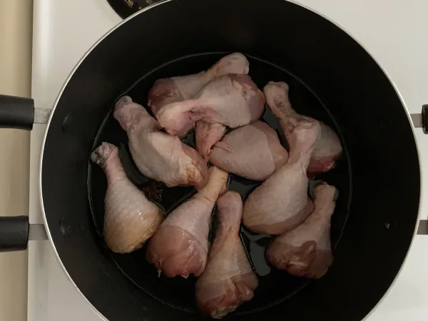 Pale pink, uncooked chicken drumsticks sit in a black pot. A small amount of dark liquid is visible in the pot.