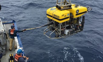 A crane on a boat holds a remotely operated vehicle (ROV) over the water as it is deployed.