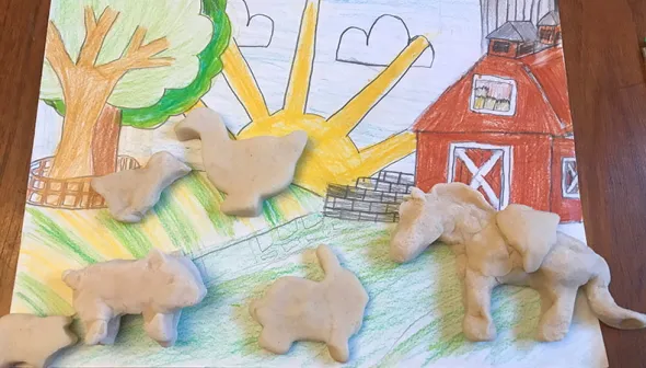 Une variété de formes d'animaux en pâte à modeler sont placées sur une scène de ferme colorée dessinée à la main.