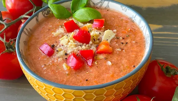 A bowl of gazpacho garnished with diced tomatoes and red peppers, fresh basil and croutons.