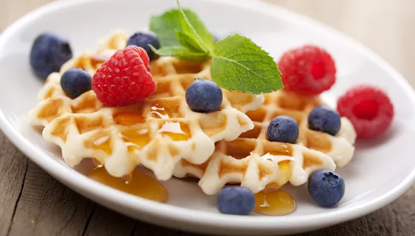 A plate of waffles is topped with blueberries, raspberries, and syrup.