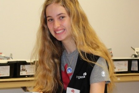 Une jeune femme portant une veste et un porte-nom sourit à la caméra.