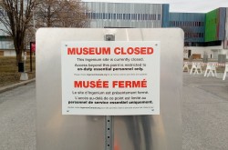 A sign in front of the barricaded museum buildings reads: “MUSEUM CLOSED…Access beyond this point is restricted to on-duty essential personnel only.”
