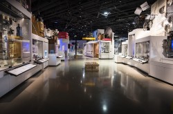 A wide-angle photo shows the Artifact Alley exhibition within the Canada Science and Technology Museum. A variety of artifacts are visible in cases on both sides of the image. 