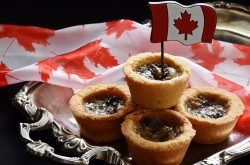 A stack of butter tarts sit on a silver platter; a small Canadian flag is inserted into the top butter tart.