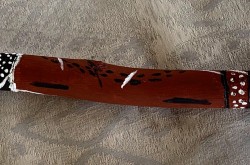 Un bâton utilisé dans des cérémonies, peint en brun et portant des motifs blancs et noirs.