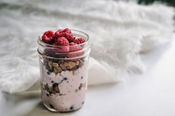 A mason jar filled with yogurt, granola, and raspberries.