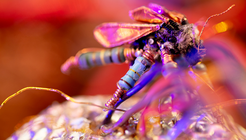 A close-up of a dragonfly fashioned out of wires and beads, set against a bright red background.