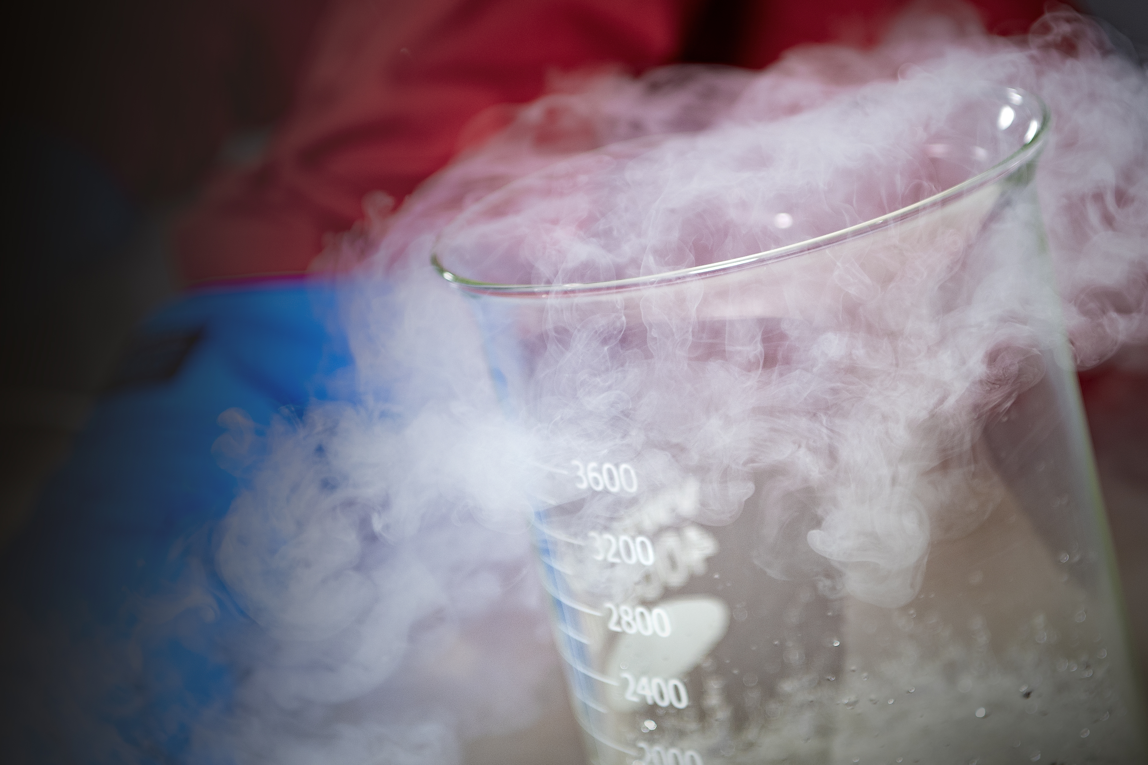 A close up shot of liquid nitrogen flowing out of a glass beaker. 
