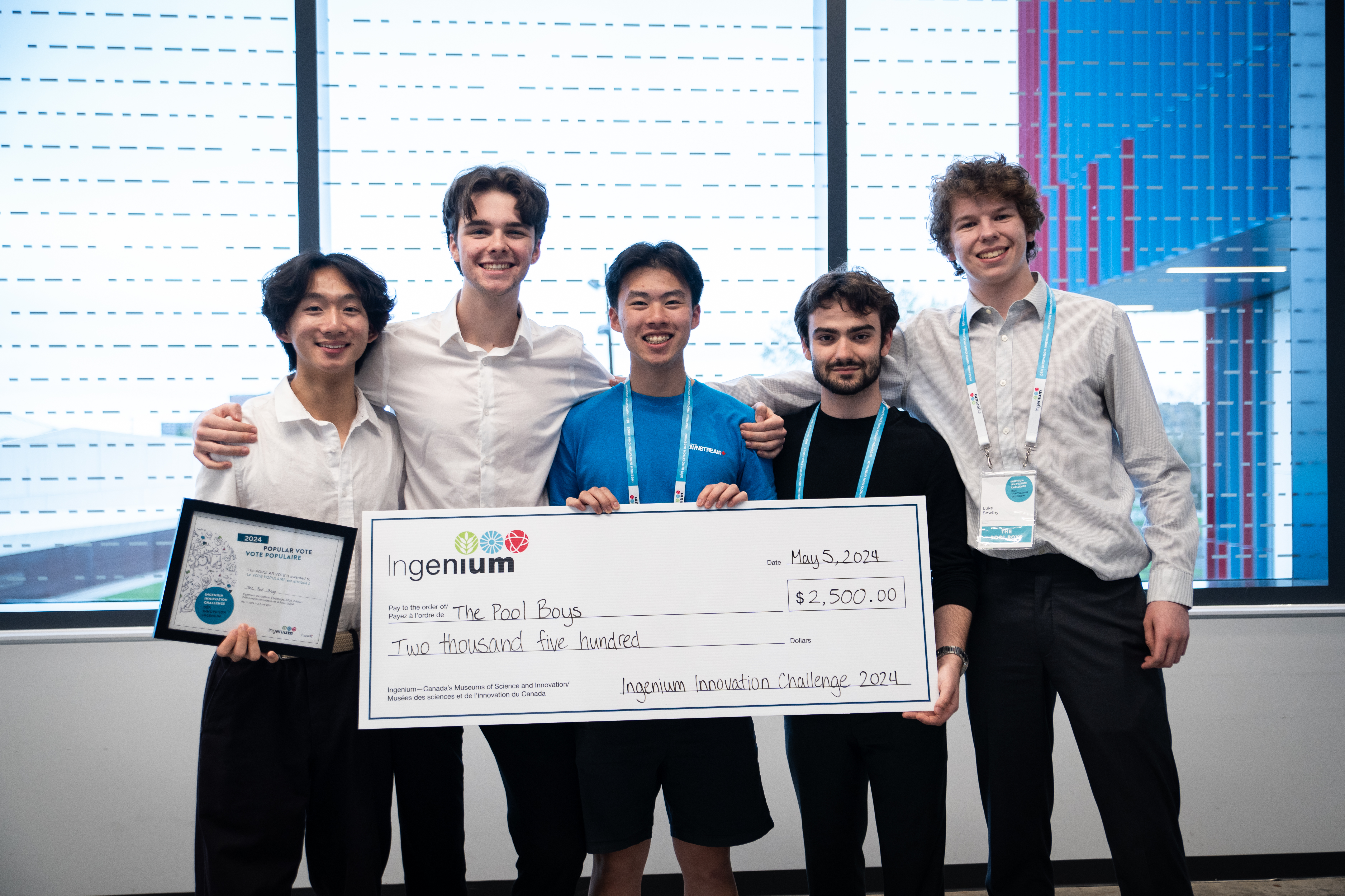 A group of five young male adults smiling, holding an oversized cheque for the amount of $2,500. 