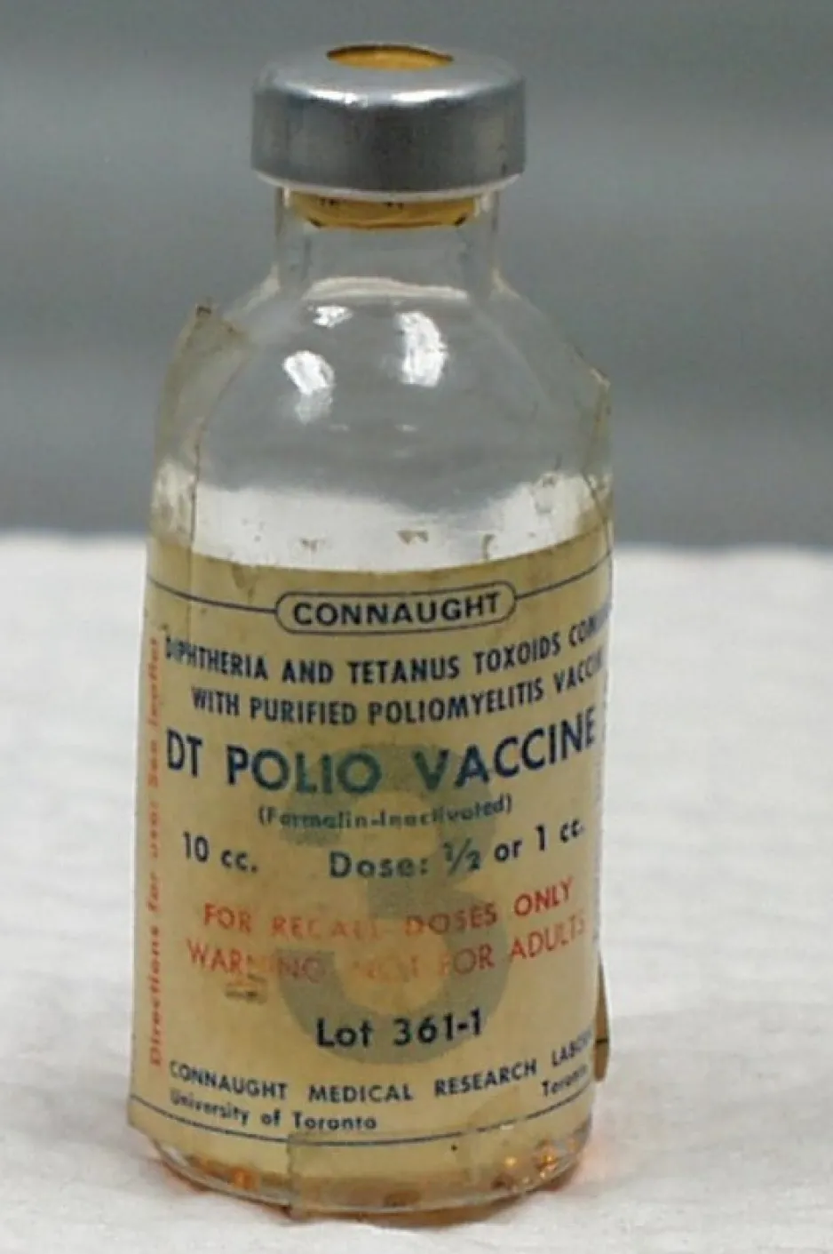 A small, empty, glass vial with a faded label that reads, “DT Polio Vaccine”.