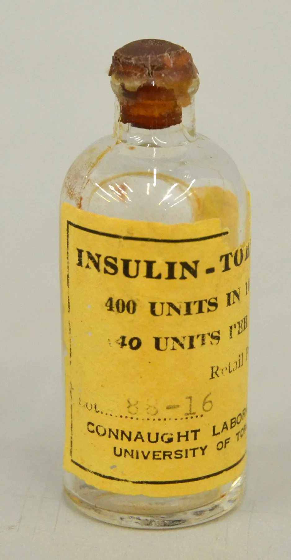 A small glass bottle has a bright yellow label; the word “Insulin” is clearly visible in black lettering. The words “400 units, 40 units” are partially visible at the top of the label, and “Connaught Laboratory, University of Toronto” is partially visible at the bottom of the label.