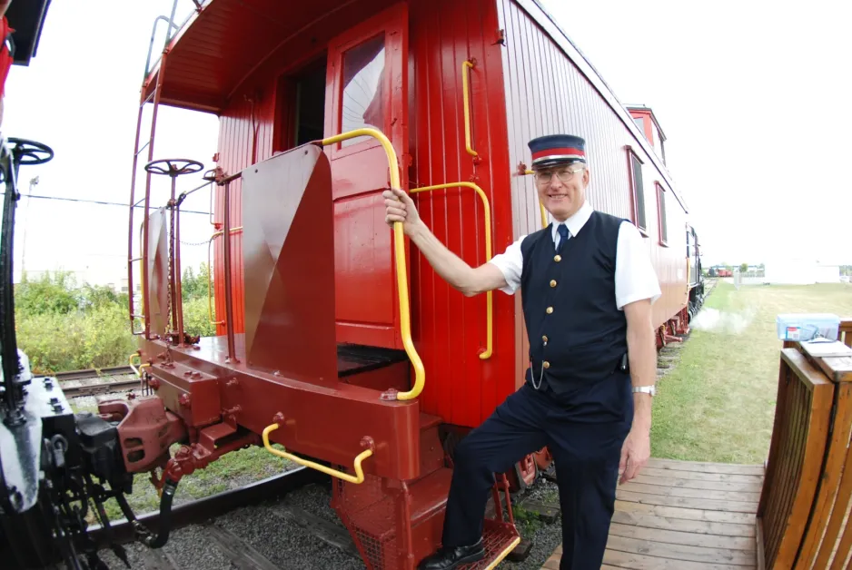 Phillip Jago, a long time volunteer with the Bytown Railway Society, stand next to a train car in a conductors uniform.