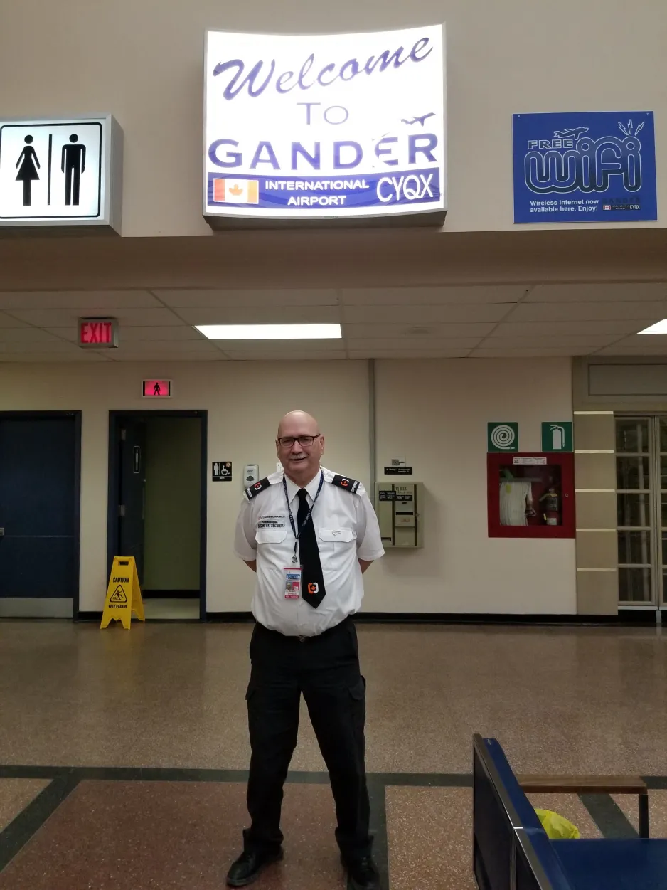 Notre guide Jerry Cramm se tenant dans la zone internationale devant un panneau "Bienvenue à Gander".