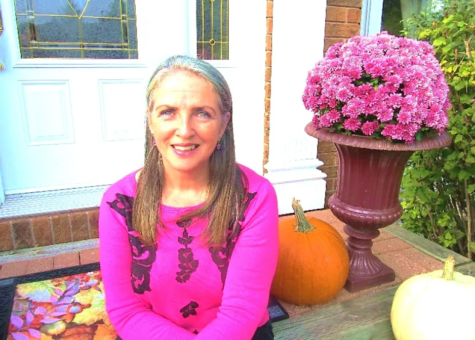 2)	Dawn Nicholson-O’Brien sits on a doorstep next to a pot of pink flowers.