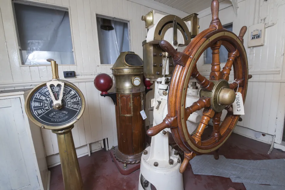 A view of the steering wheel and other pieces of equipment, inside the wood-panelled walls of the pilot house.