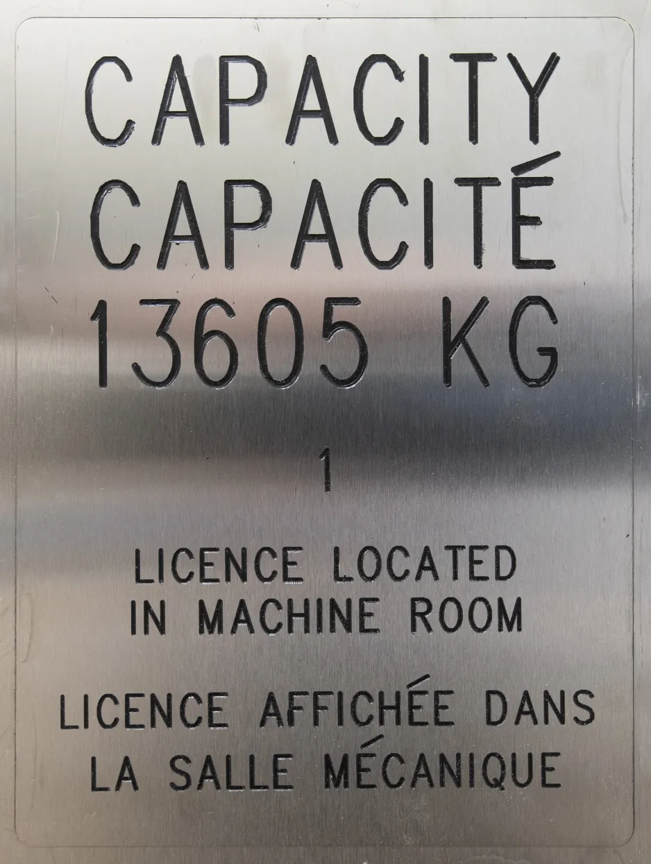 A close-up of a silver panel in the freight elevator indicates the maximum capacity is 13,605 kg.