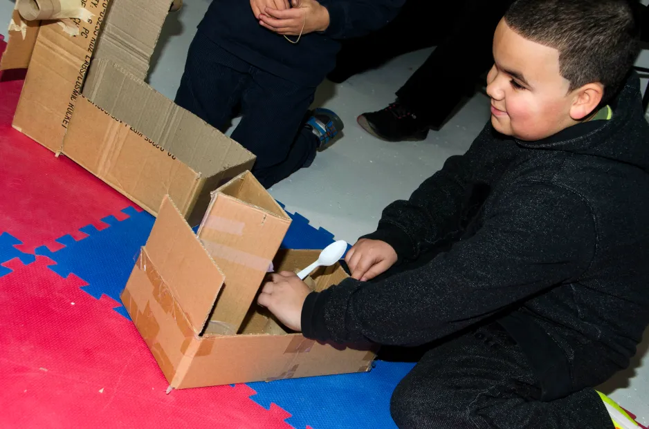 Un garçon joue avec une catapulte fabriquée à partir d’une boîte de carton.
