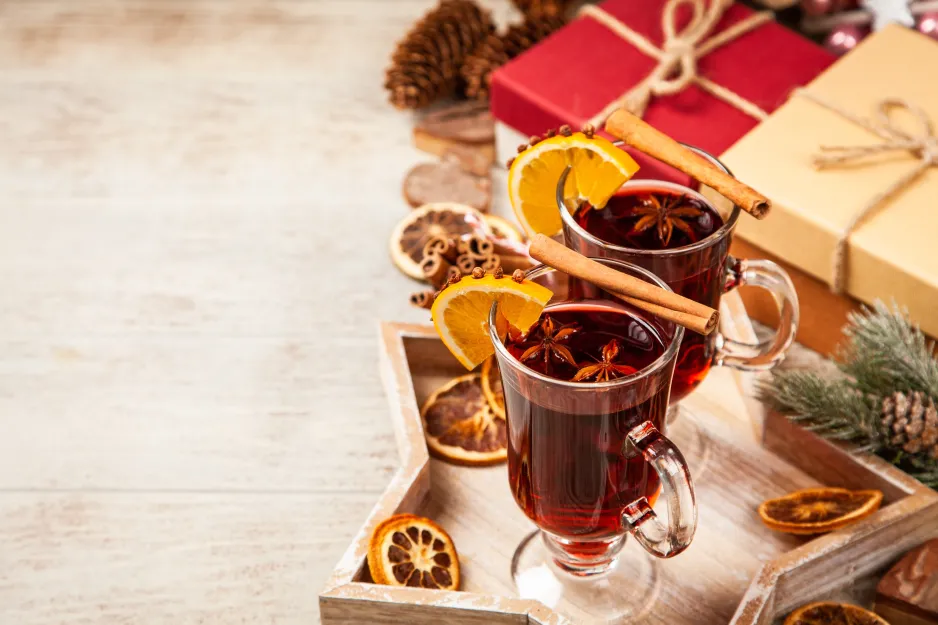 Deux verres décoratifs remplis de vin chaud et posés sur un plateau à côté de cadeaux de Noël