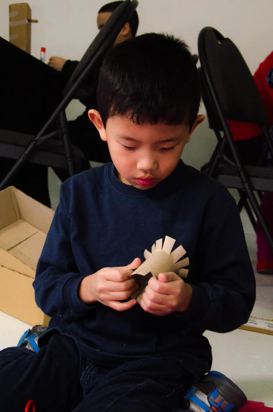 A boy cuts flanges into a toilet paper roll and surveys his work