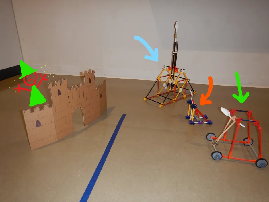 A display of several K’NEX catapults lined up next to a cardboard castle target