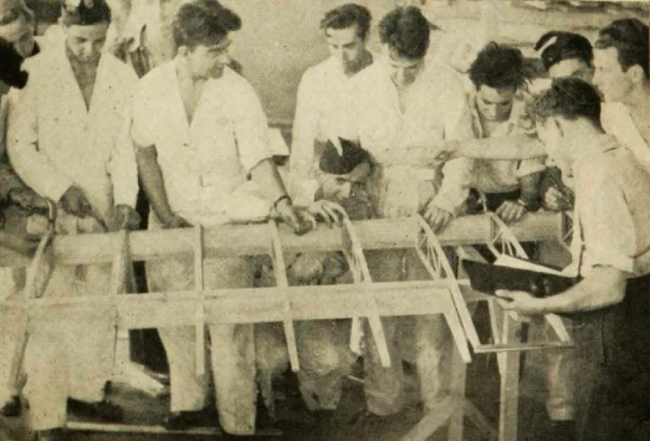 A group of men are gathered around the inner wooden structure of an airplane wing.