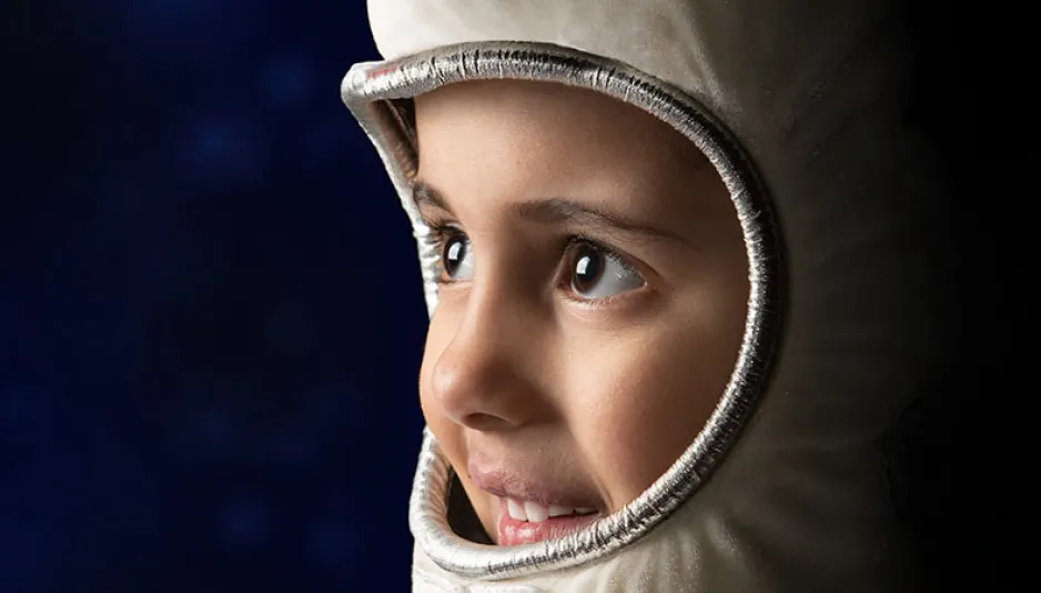 La silhouette d’un jeune enfant sourit et regarde à travers un costume d’astronaute. 