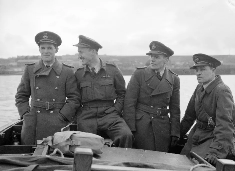 A black-and-white image shows four young men in military uniform, side by side on a boat.