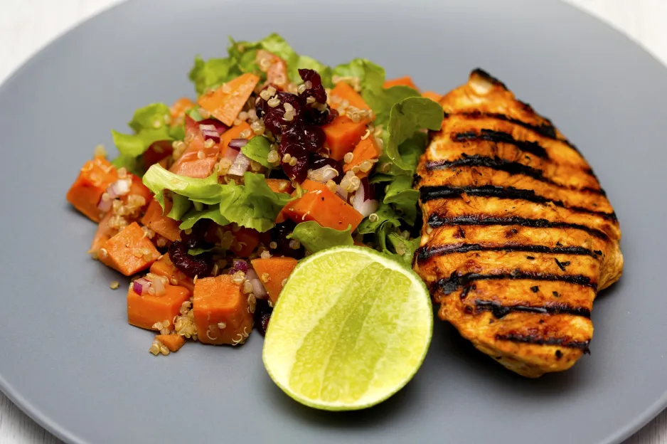 A plated meal of grilled chicken, a quinoa salad, and a lime garnish. 